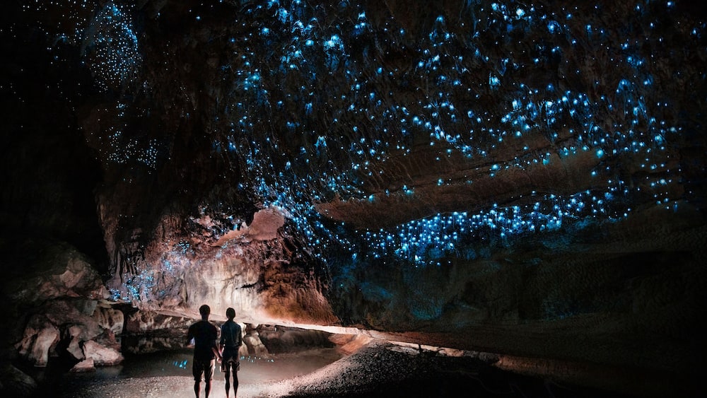 Two people walking through a cave with bioluminescent blue lights.