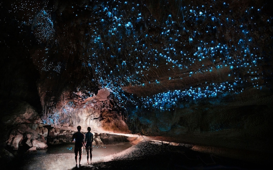 Duas pessoas caminhando por uma caverna com luzes azuis bioluminescentes.