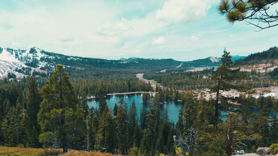 A mountainous landscape with a lake, dense forests, and snow-capped peaks.