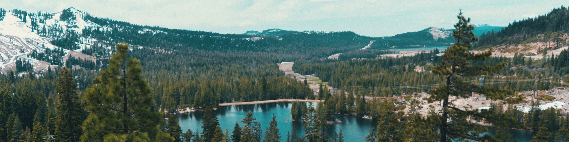 Un paisaje montañoso con un lago, bosques densos y picos nevados.