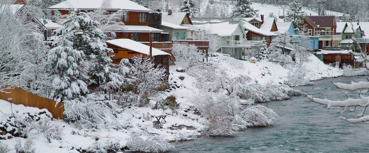 A snow-covered riverbank with houses and trees.