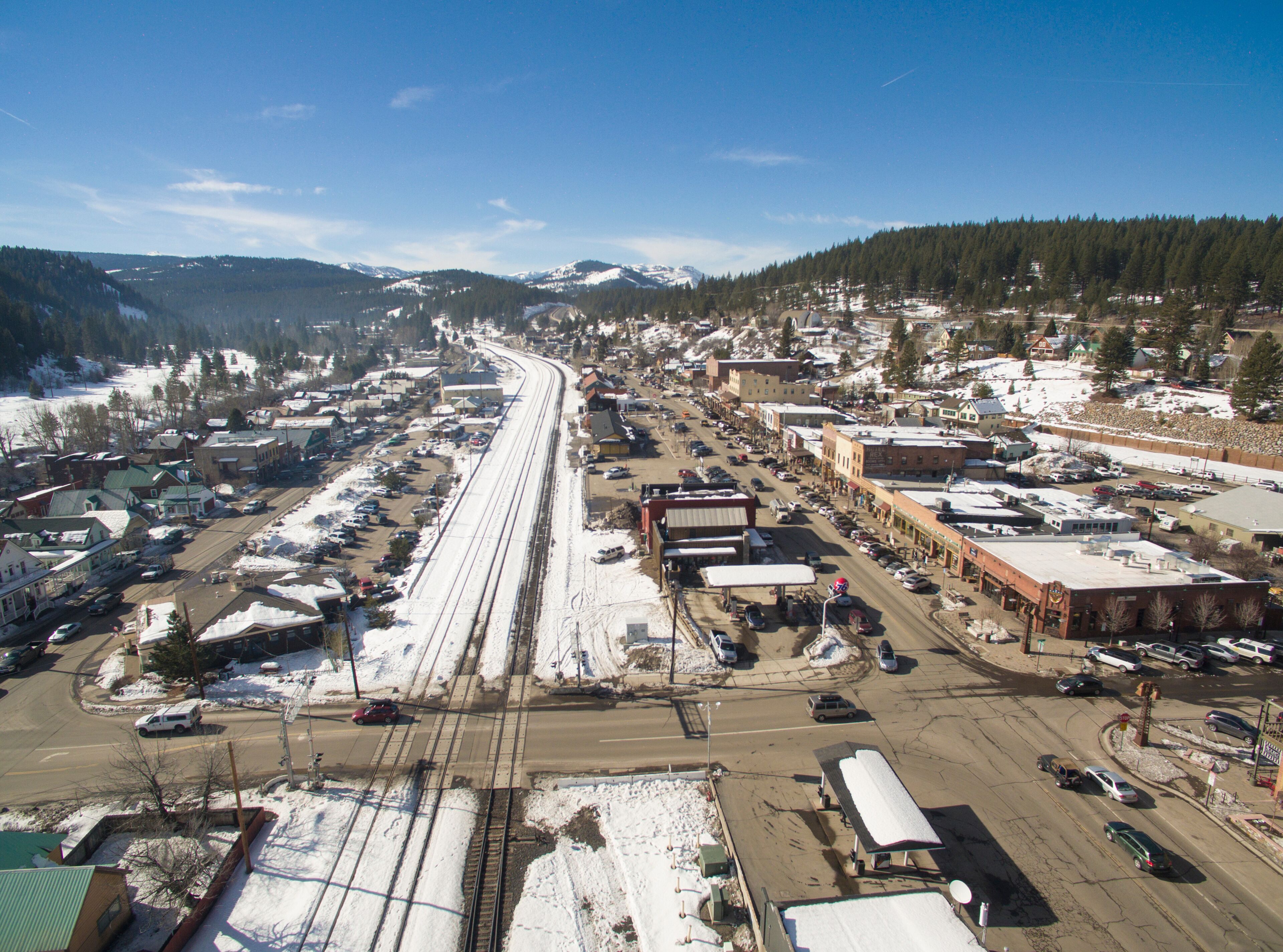 A snowy town with a railway track, buildings, and a mountainous backdrop.