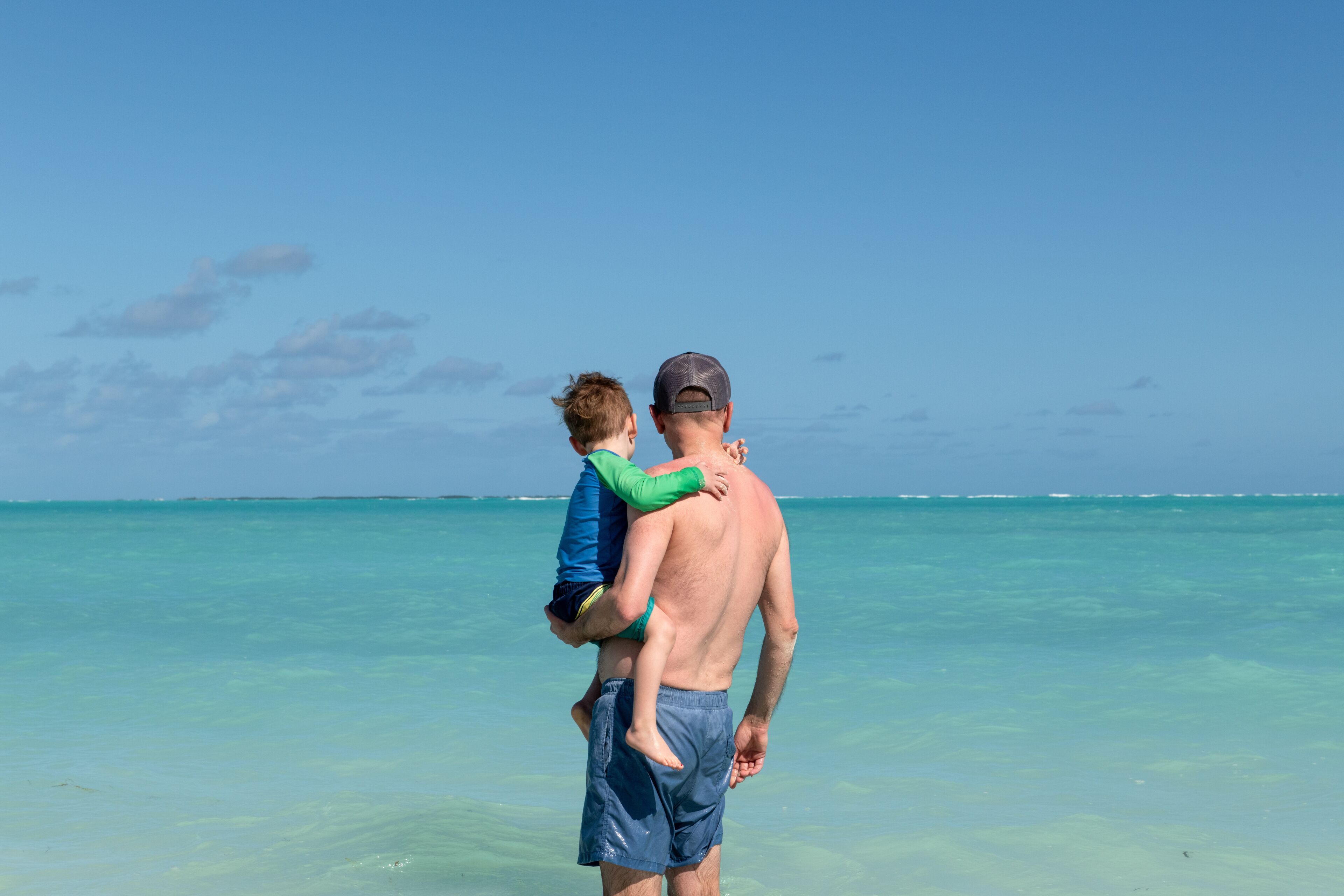 Father carries young son into the blue-green water of the Sea of Abaco