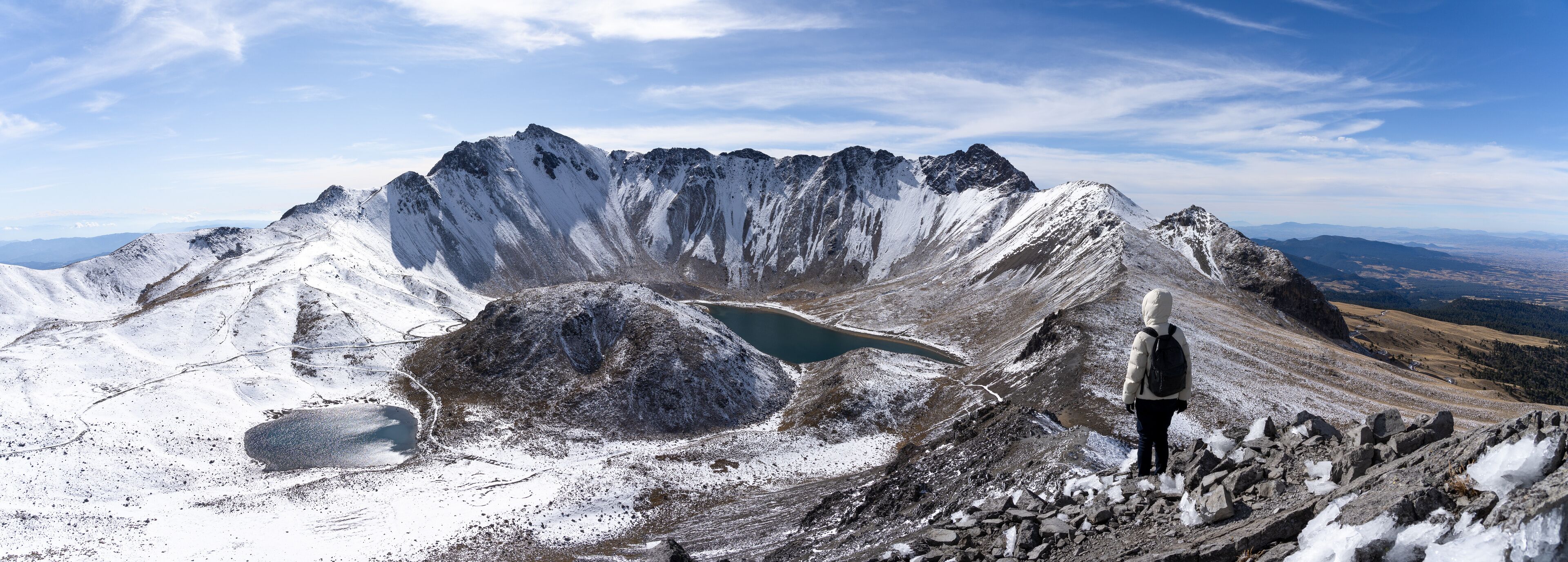 Un pico nevado de montaña con una persona de pie sobre un saliente rocoso.