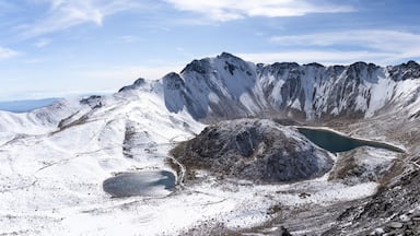 Un pico nevado de montaña con una persona de pie sobre un saliente rocoso.