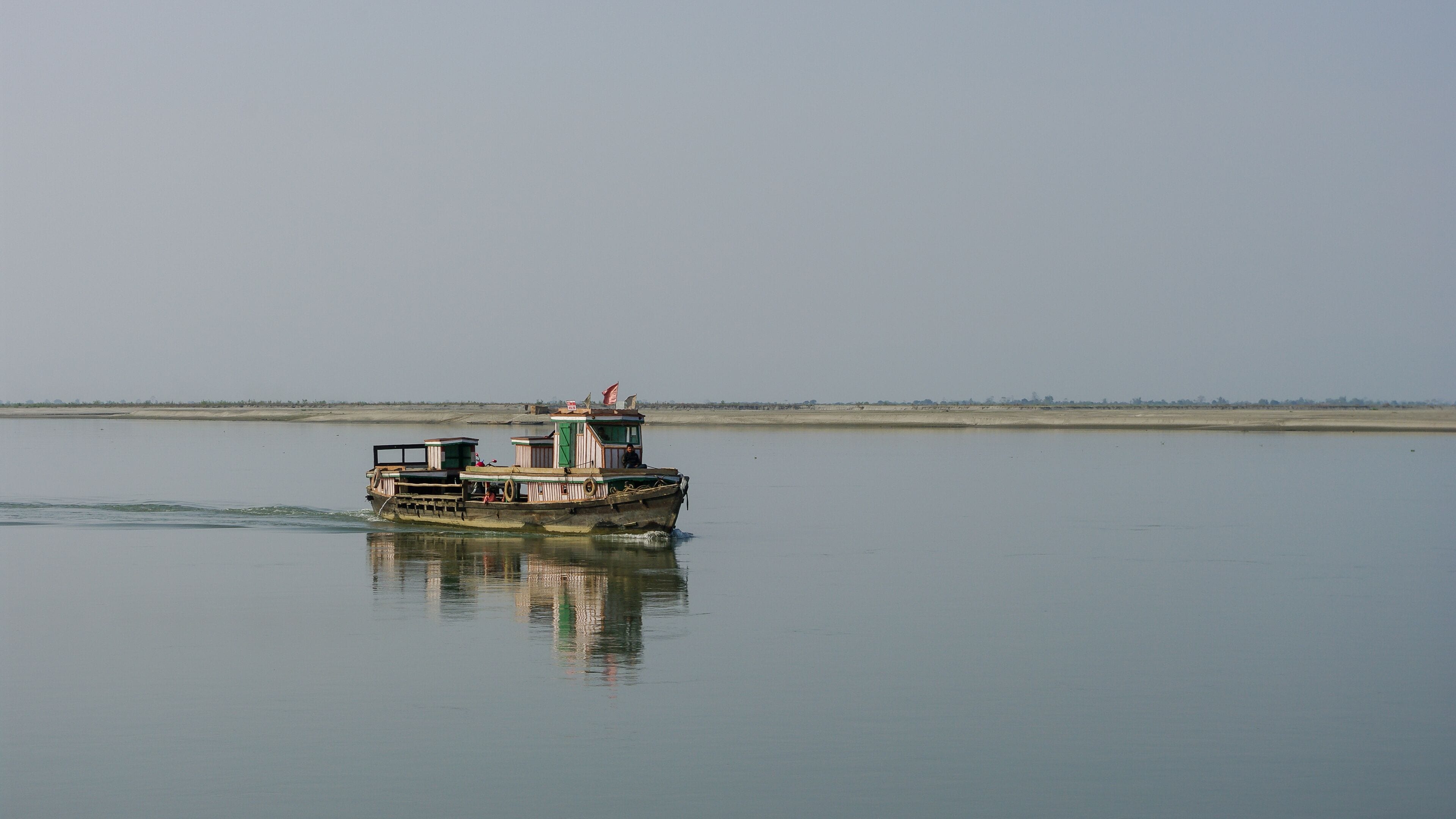 Scenic landscape view of small wooden ferry boat crossing the mighty Brahmaputra river in Assam, India