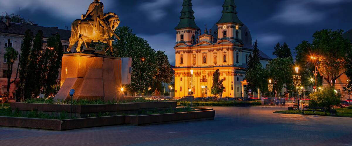 A statue of a man on horseback, a church with two spires, and a well-lit square.