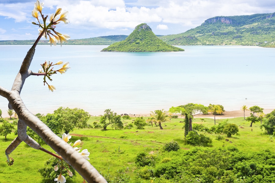 Un paysage verdoyant et luxuriant, avec une étendue d’eau importante, une petite île et une montagne en arrière-plan.