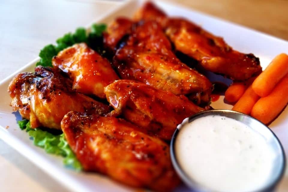 A plate of chicken wings with a side of carrots and a dipping sauce.
