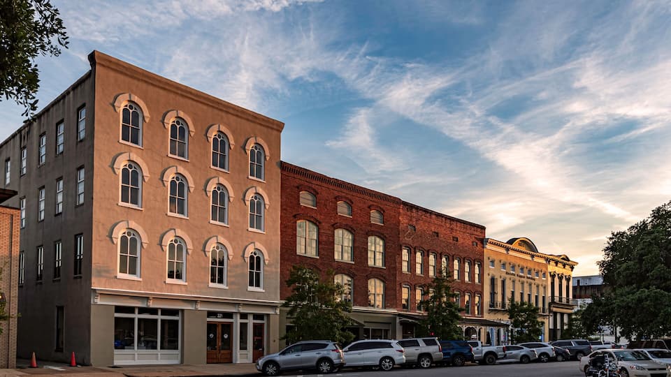 A street lined with historic buildings, parked cars, and a clear sky.