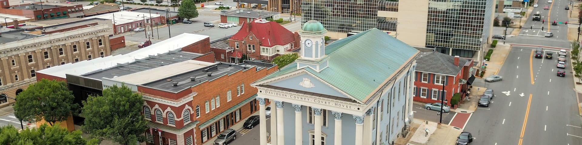 A cityscape with a prominent courthouse, a mix of historic and modern buildings, and a clear road with vehicles.