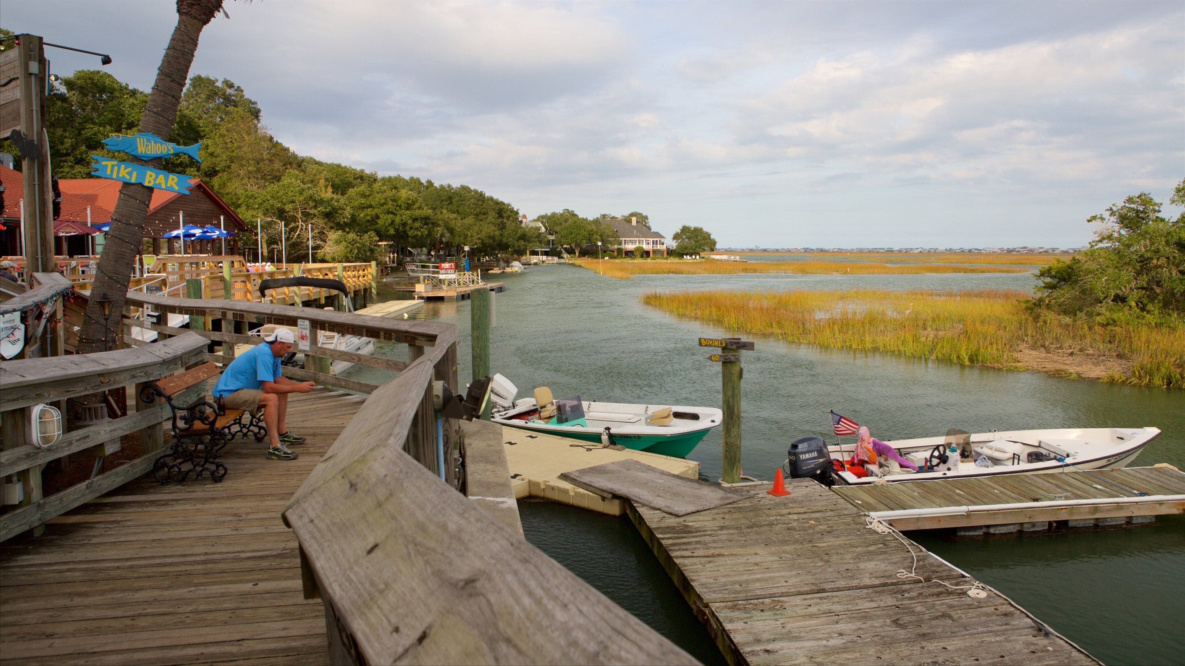 A wooden dock with boats, a tiki bar, and a sign for Wahoa's.