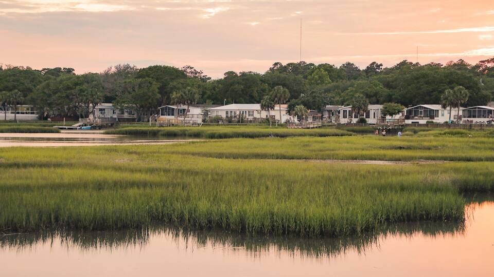 A coastal landscape with houses, a calm water body, and dense greenery.