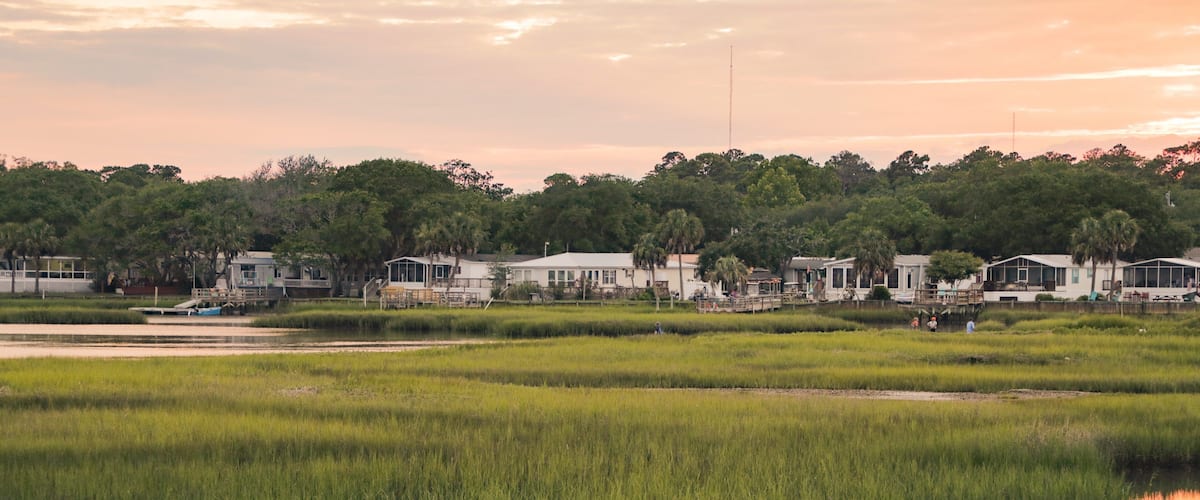 A coastal landscape with houses, a calm water body, and dense greenery.