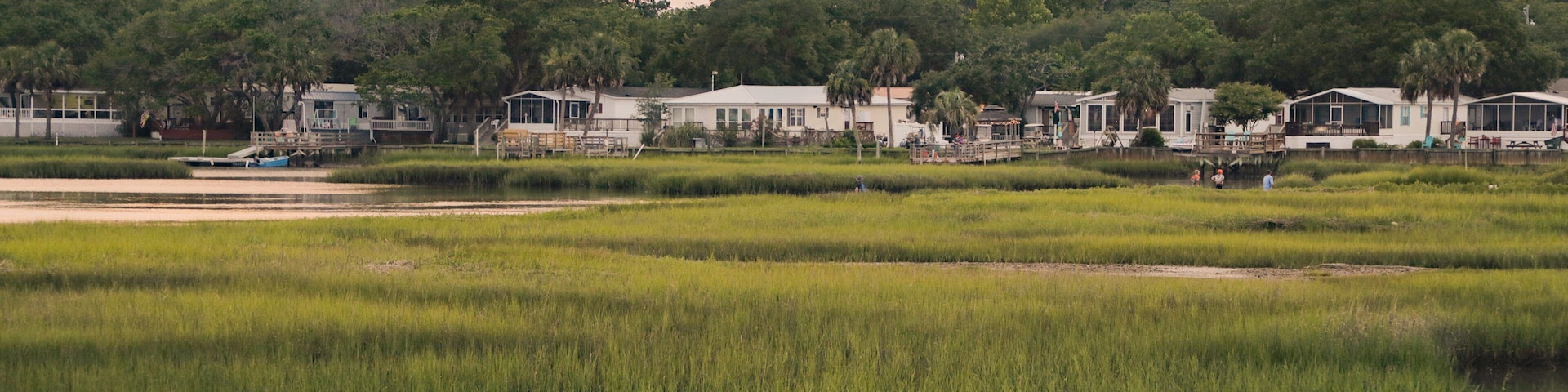 A coastal landscape with houses, a calm water body, and dense greenery.