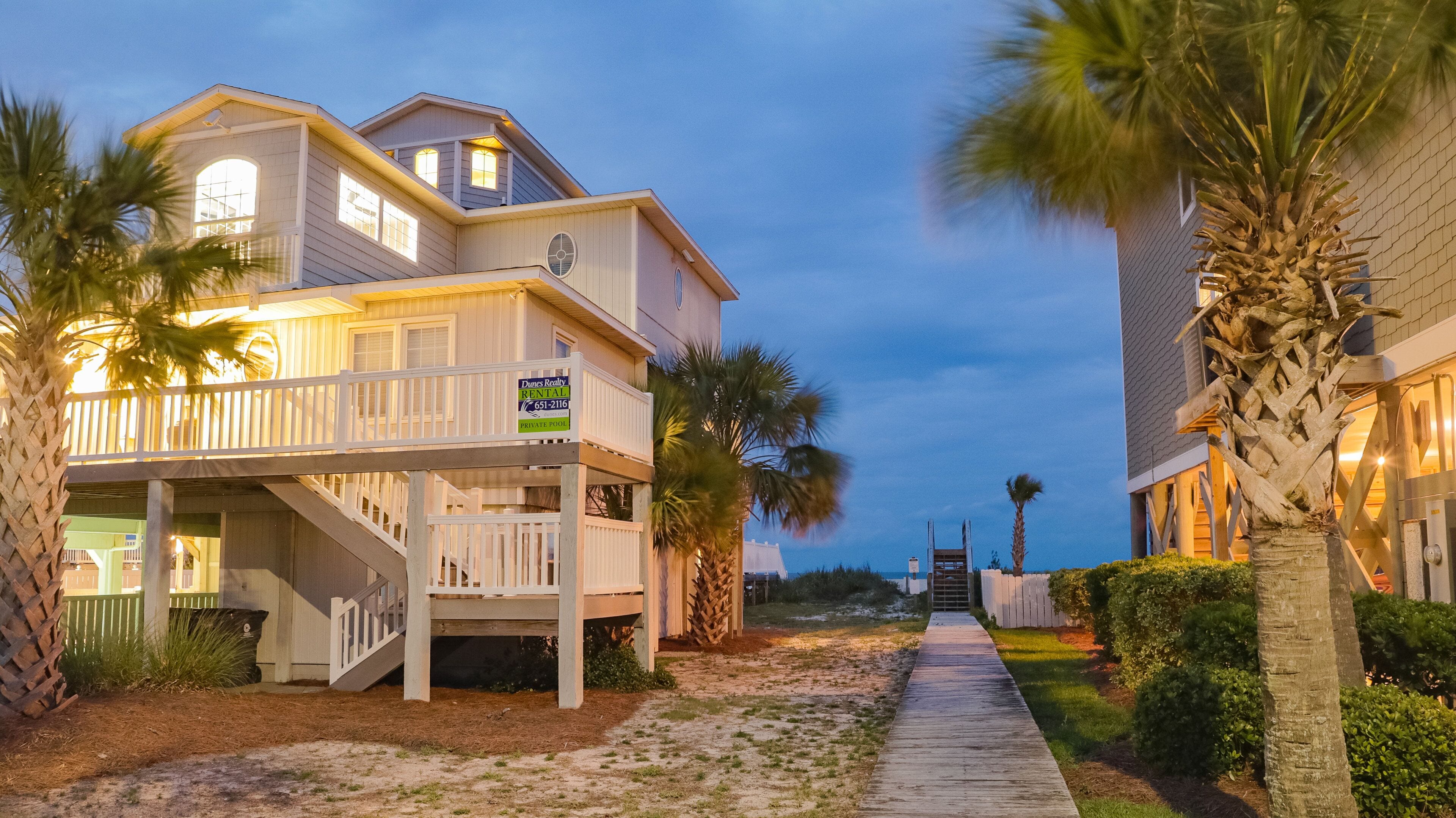A beachfront property with a two-story house, a private pool, and a wooden walkway.