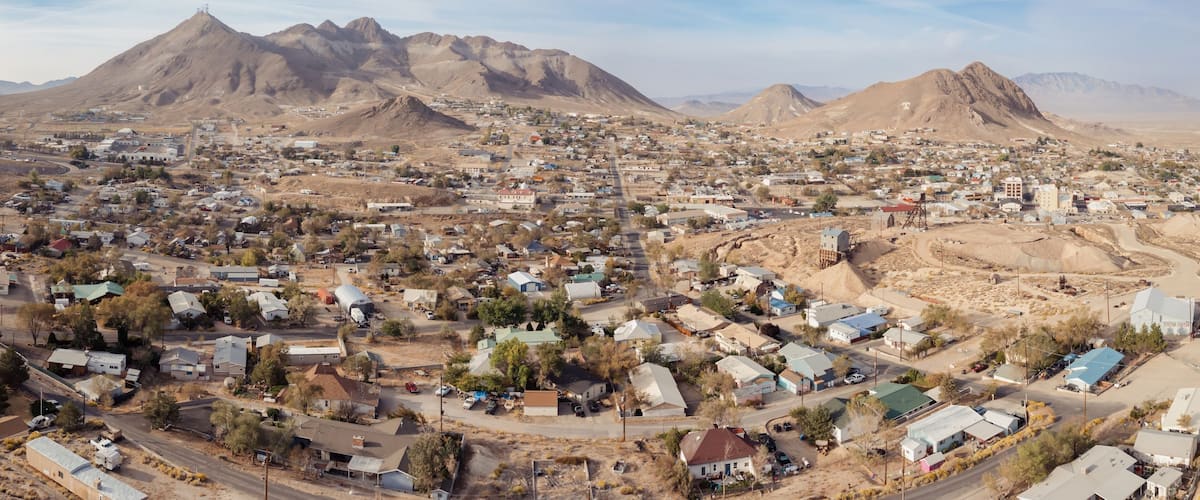 A town with a mountainous backdrop, featuring a mix of residential and commercial buildings, a prominent church, and a large water tower.
