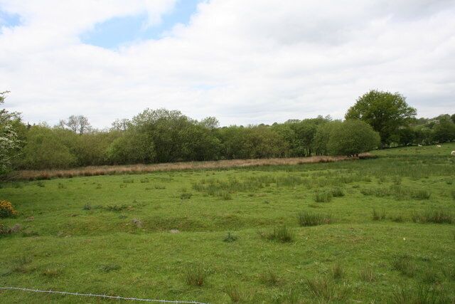 A green field with a fence, trees, and a cloudy sky.