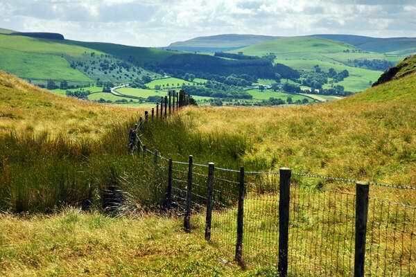 A grassy hillside with a wooden fence and a valley in the background.
