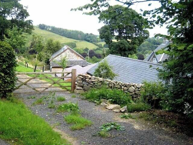 Paisaje rural con un muro de piedra, una puerta de madera y casas con techos inclinados.
