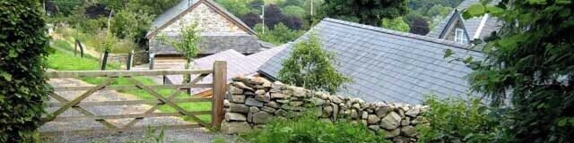 Paisaje rural con un muro de piedra, una puerta de madera y casas con techos inclinados.