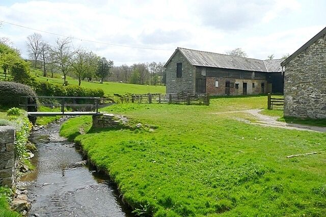 A rural landscape with a stone barn, a small stream, and a grassy field.
