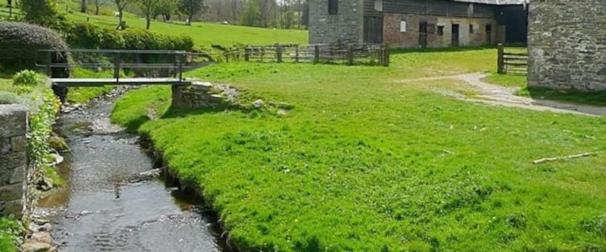 A rural landscape with a stone barn, a small stream, and a grassy field.