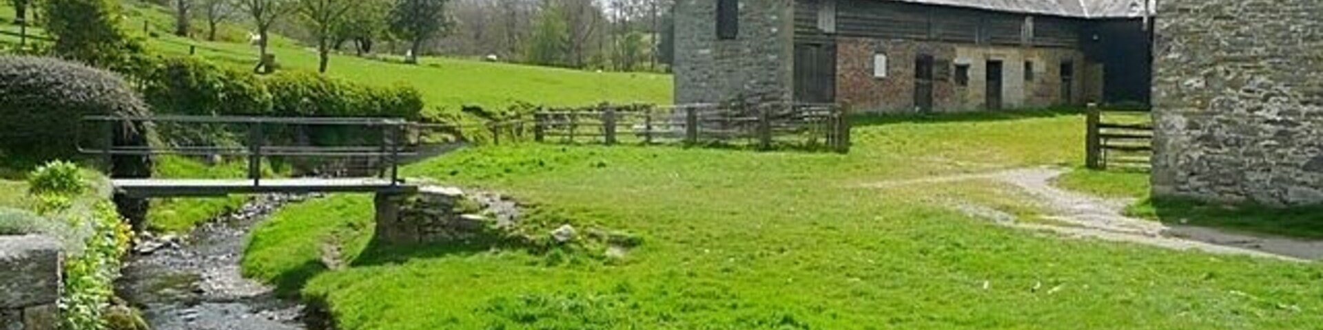 A rural landscape with a stone barn, a small stream, and a grassy field.