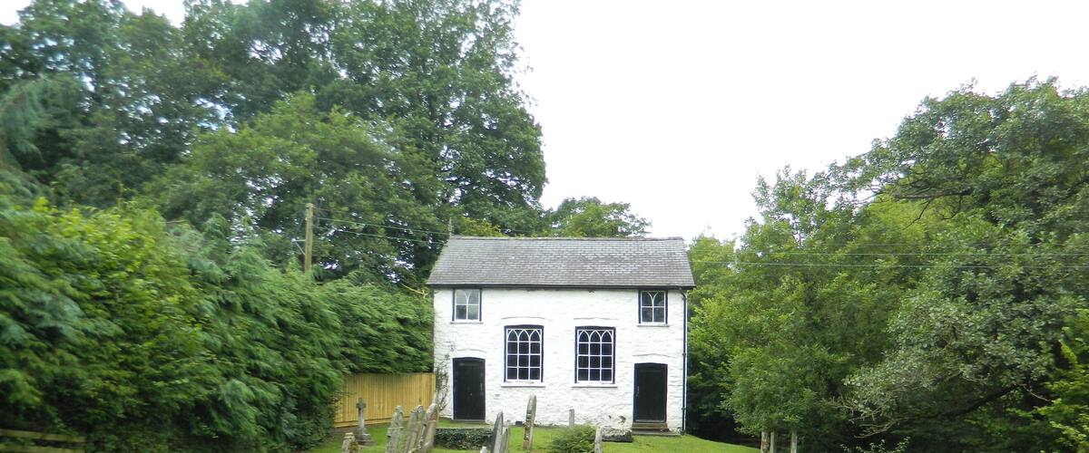 A white house with a black door and windows, surrounded by a well-maintained lawn and trees.