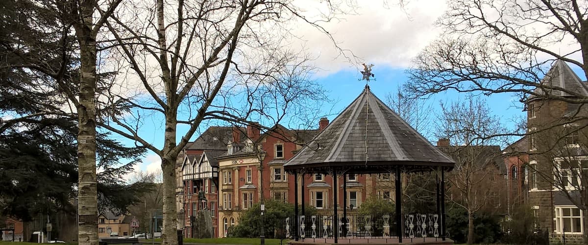 A park with a gazebo, a statue, and historic buildings.