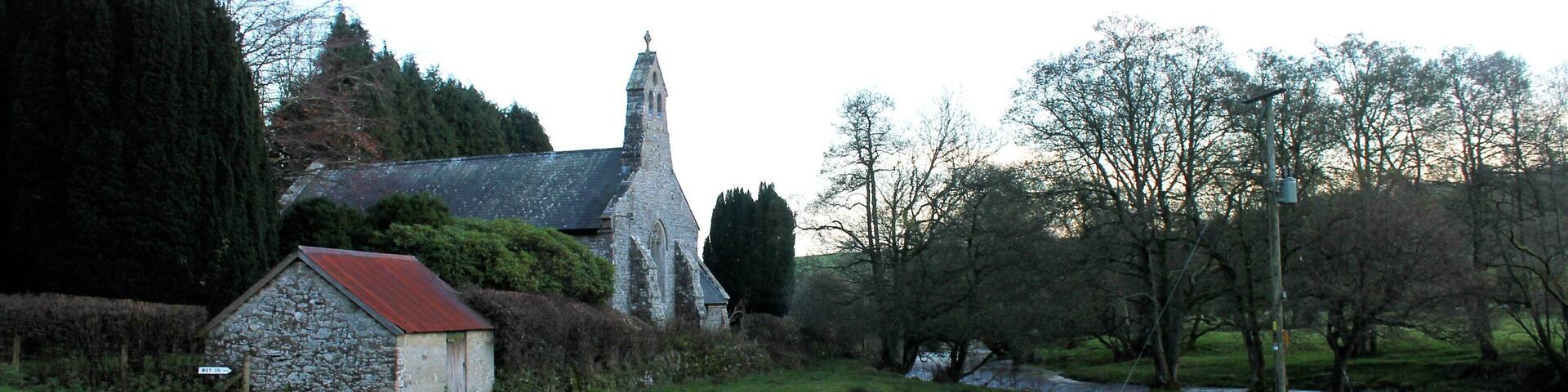 A stone church with a red roof, surrounded by a grassy field and trees.