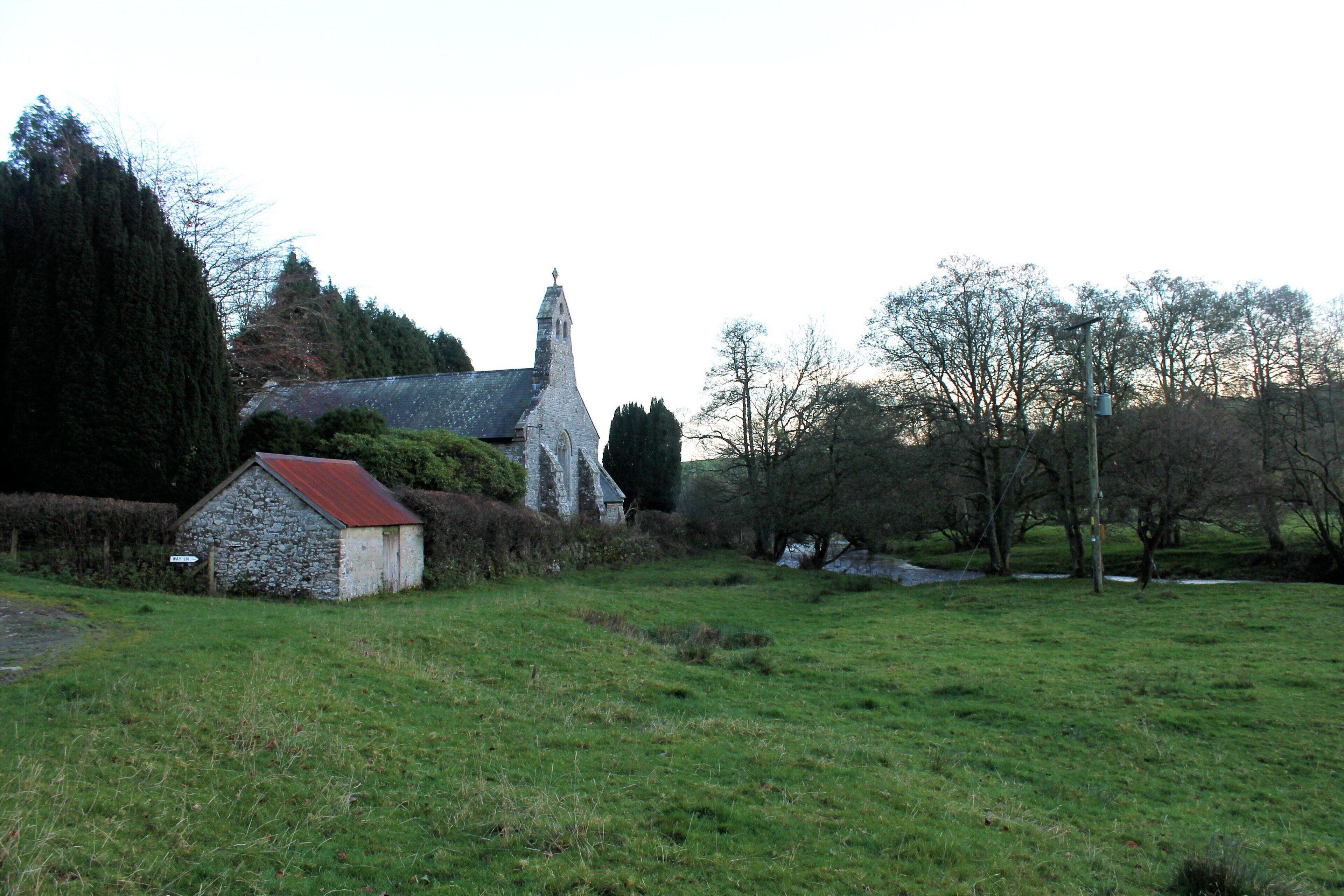 A stone church with a red roof, surrounded by a grassy field and trees.