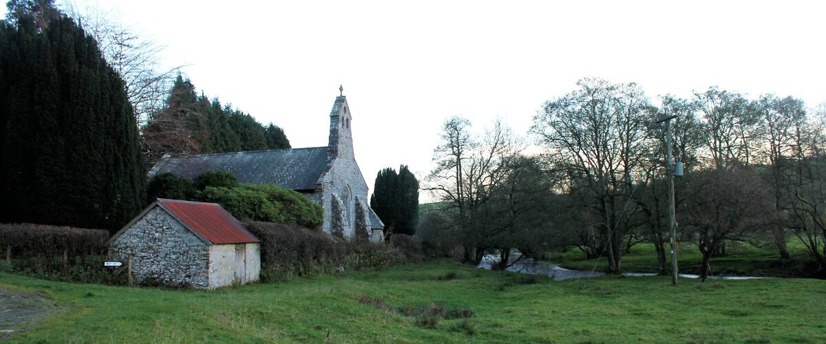 A stone church with a red roof, surrounded by a grassy field and trees.