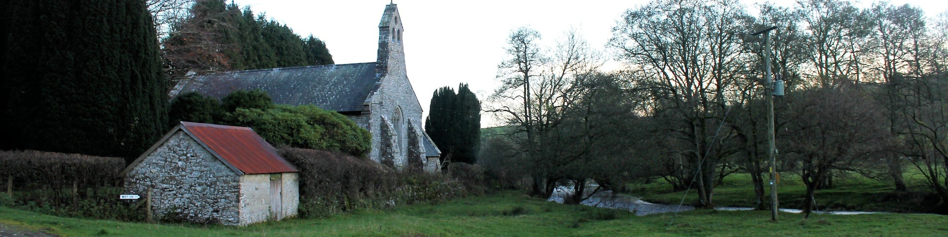 A stone church with a red roof, surrounded by a grassy field and trees.
