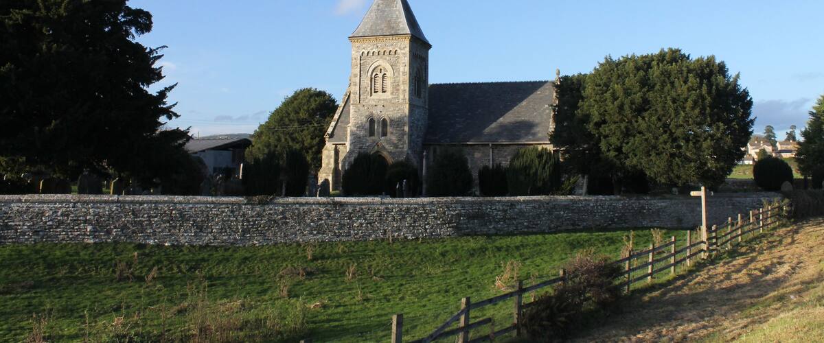A stone church with a tall tower and a stone wall in a rural setting.