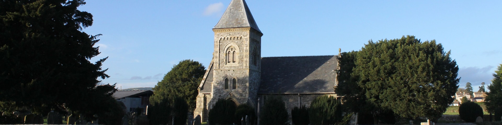A stone church with a tall tower and a stone wall in a rural setting.