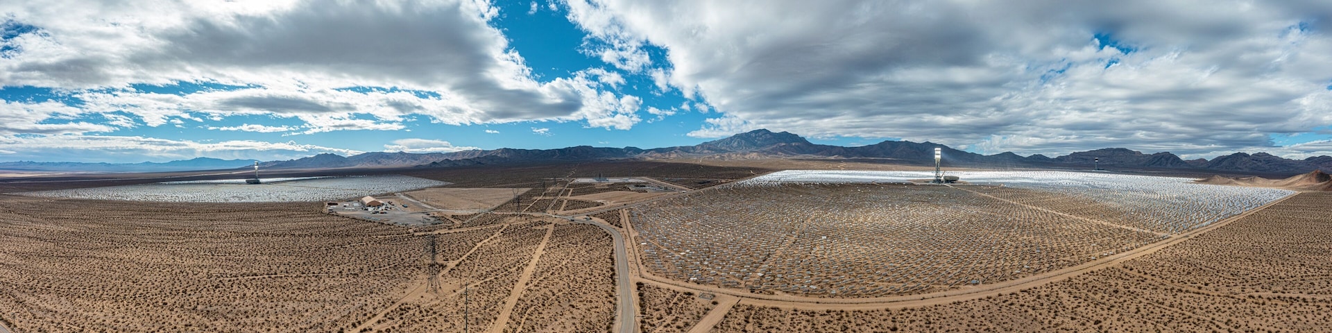 A vast desert landscape with mountains in the background, a large body of water, and a road leading through the area.