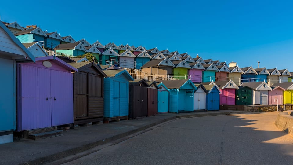 A row of colorful beach huts with pointed roofs.
