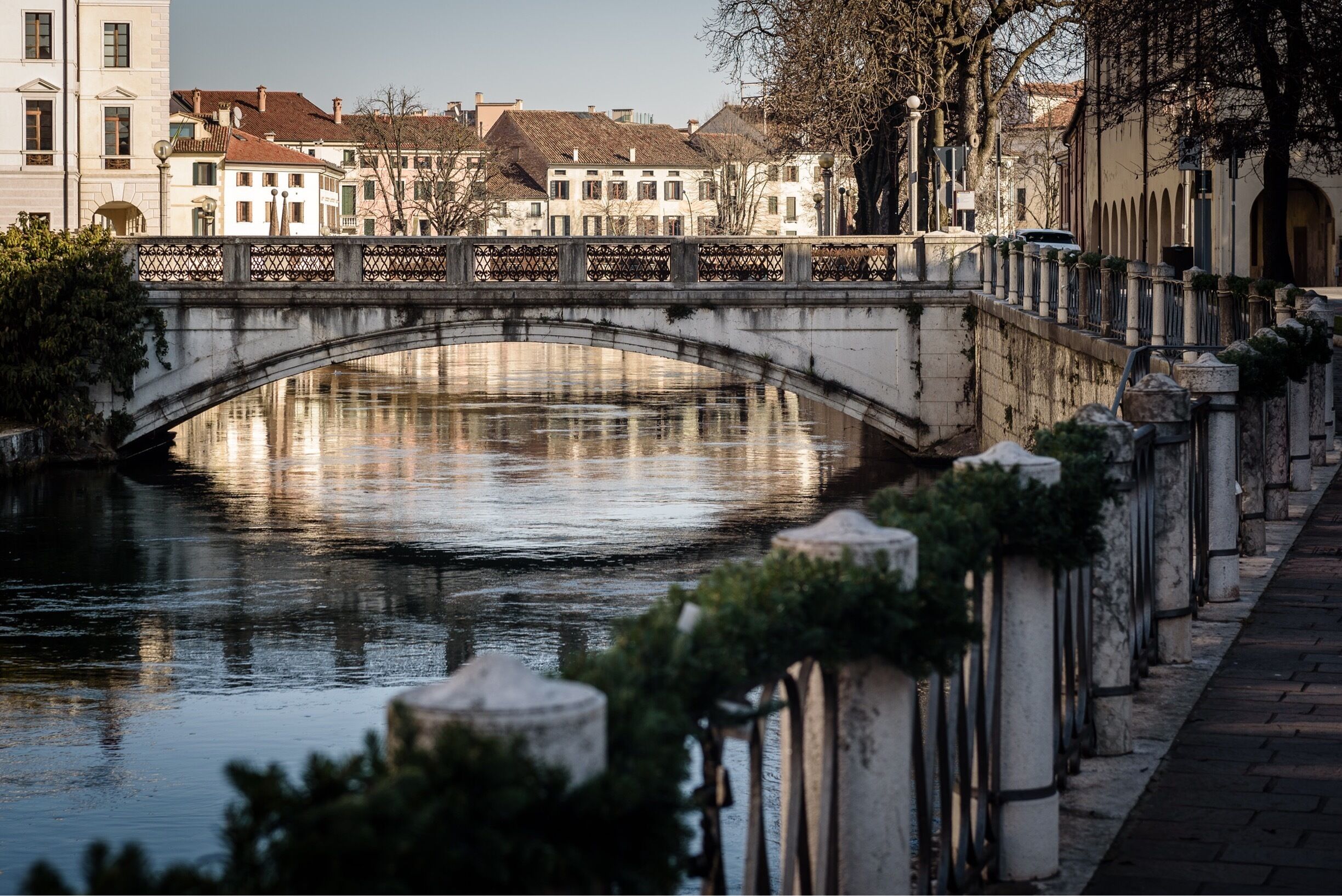 A stone bridge over a calm river, surrounded by historic buildings and trees.