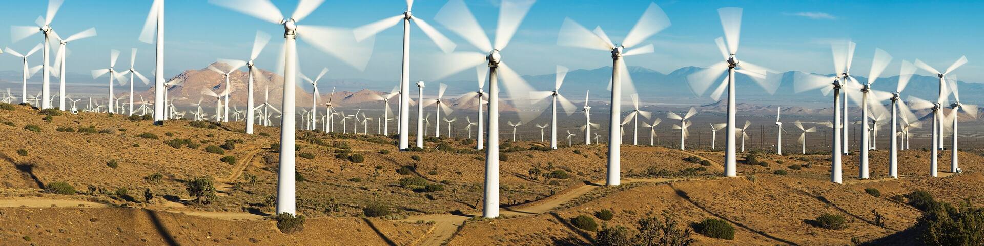 A wind farm with numerous white wind turbines on a hilly terrain under a clear blue sky.