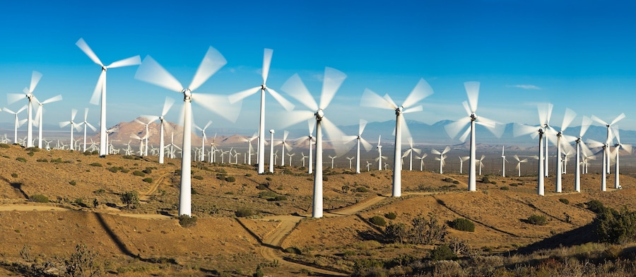 A wind farm with numerous white wind turbines on a hilly terrain under a clear blue sky.