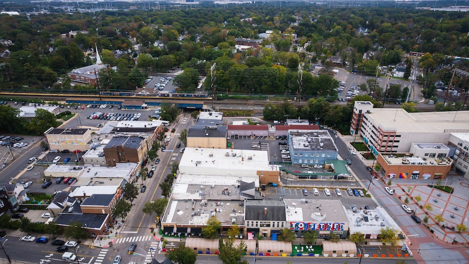 An aerial view of a city with a mix of commercial and residential buildings, a prominent church steeple, and a large parking lot.
