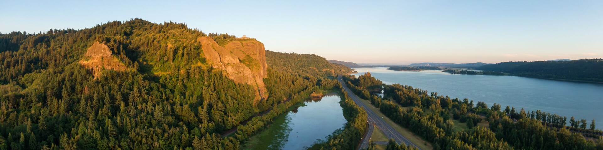 Um rio serpenteia por um vale florestado, com um afloramento rochoso proeminente à esquerda e uma estrada correndo paralelamente ao rio.