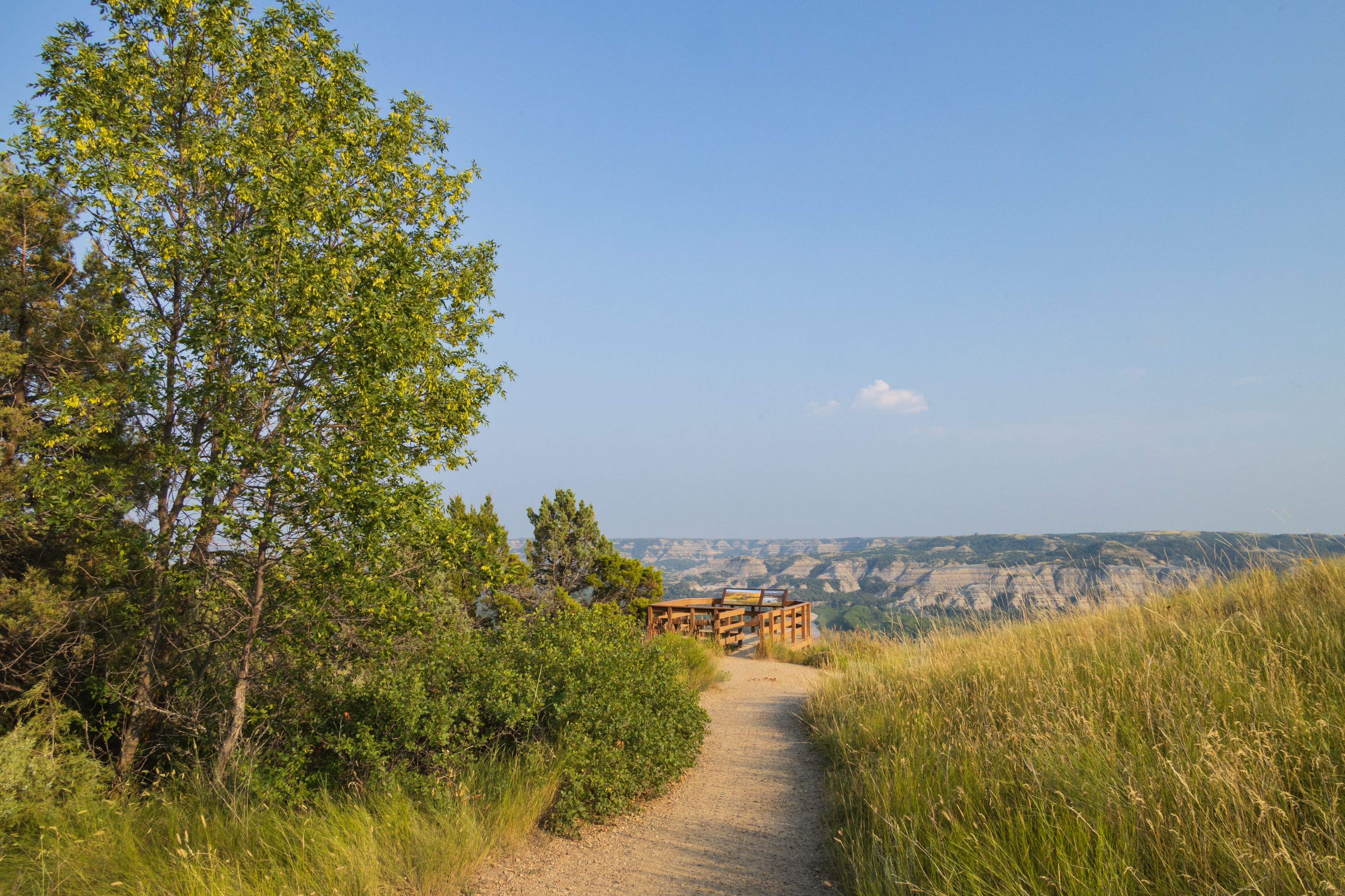 A dirt path leading to a wooden viewing platform overlooking a valley with layered rock formations.