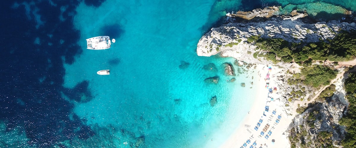 A turquoise sea with boats, a rocky coastline, and a beach with umbrellas.