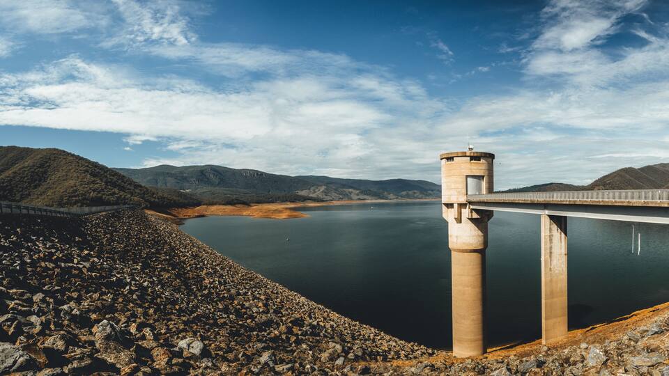A dam with a bridge, a calm lake, and surrounding hills.