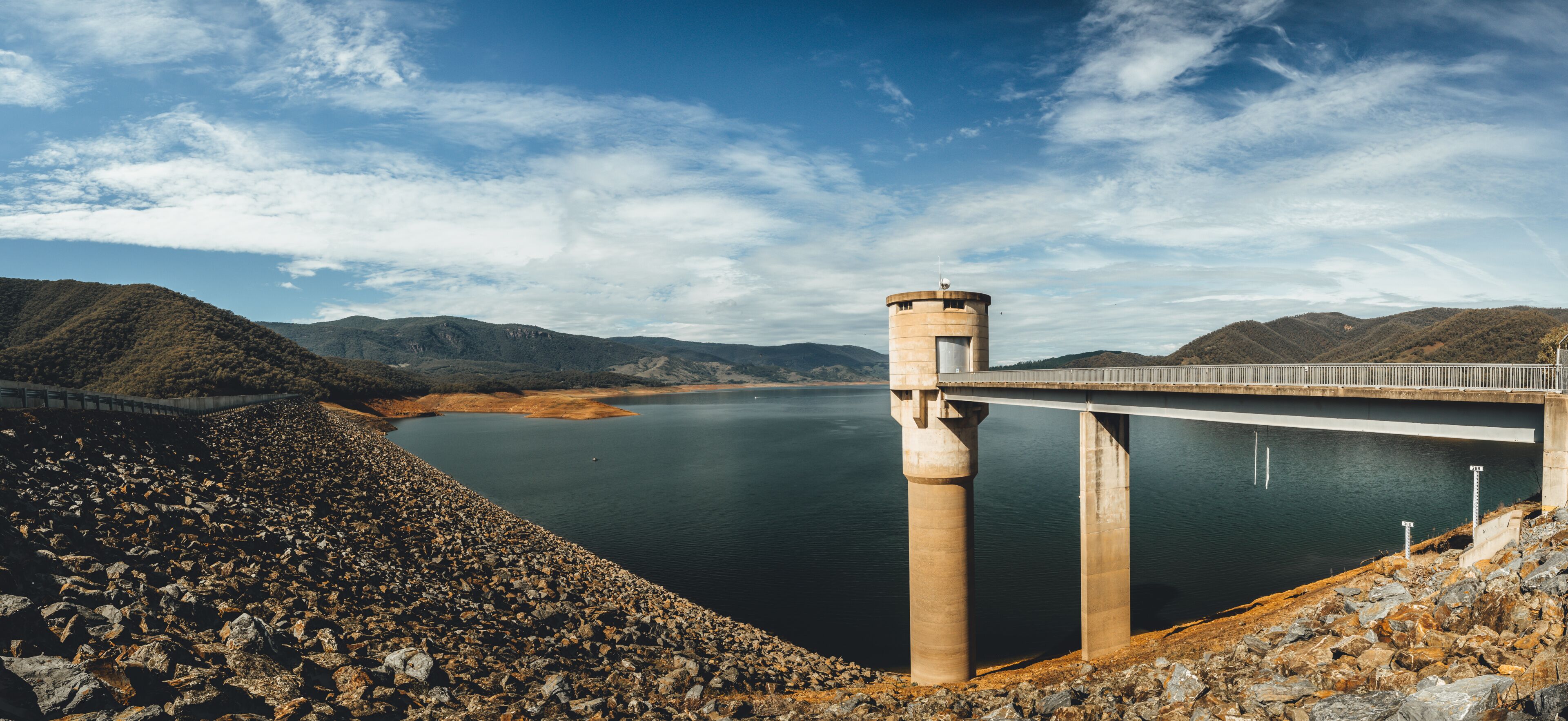 A dam with a bridge, a calm lake, and surrounding hills.