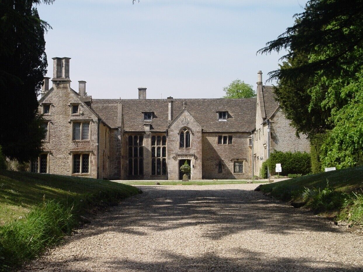 A historic stone building with a gravel driveway leading to a gated entrance.