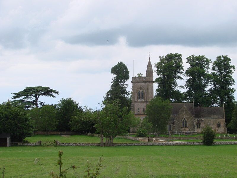 A church with a tall spire, surrounded by trees and a grassy field.