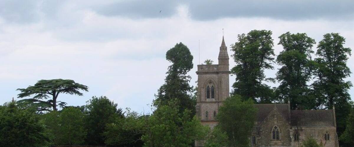 A church with a tall spire, surrounded by trees and a grassy field.